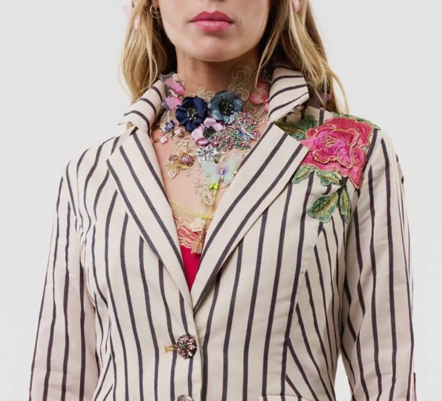 Woman in a striped blazer with floral embroidery and a lace and crystal bib necklace on a plain background