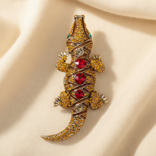 Decorative crocodile-shaped brooch with gemstones on an ivory fabric background