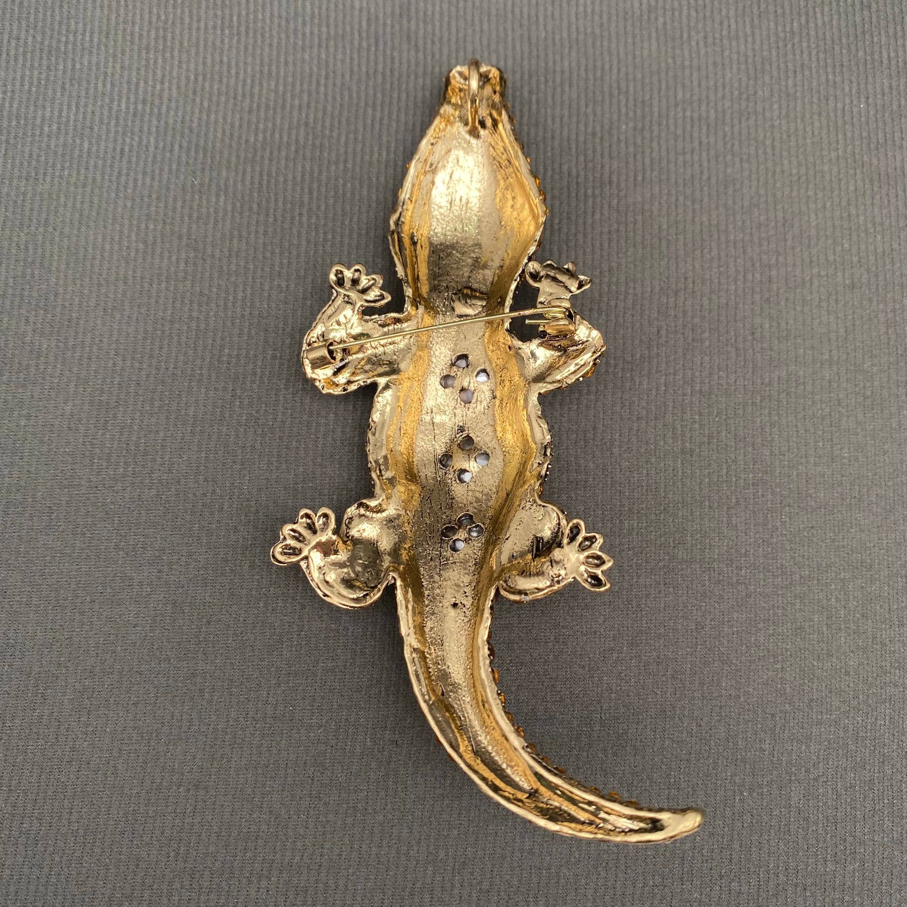 back view of gold crocodile-shaped brooch on a gray background