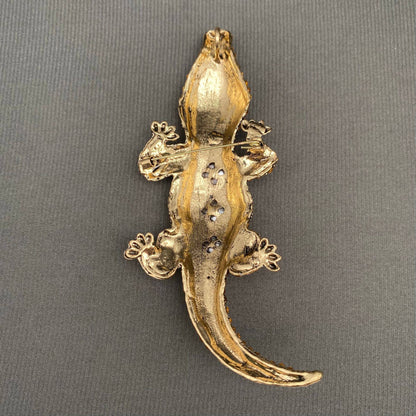 back view of gold crocodile-shaped brooch on a gray background