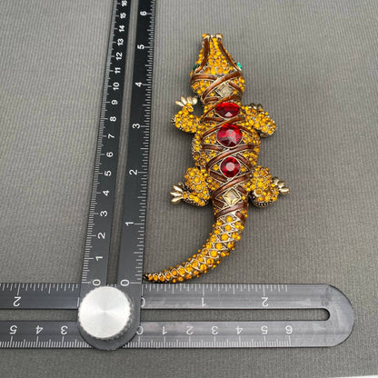Decorative crocodile-shaped object with gemstones on a gray surface with a ruler for scale.
