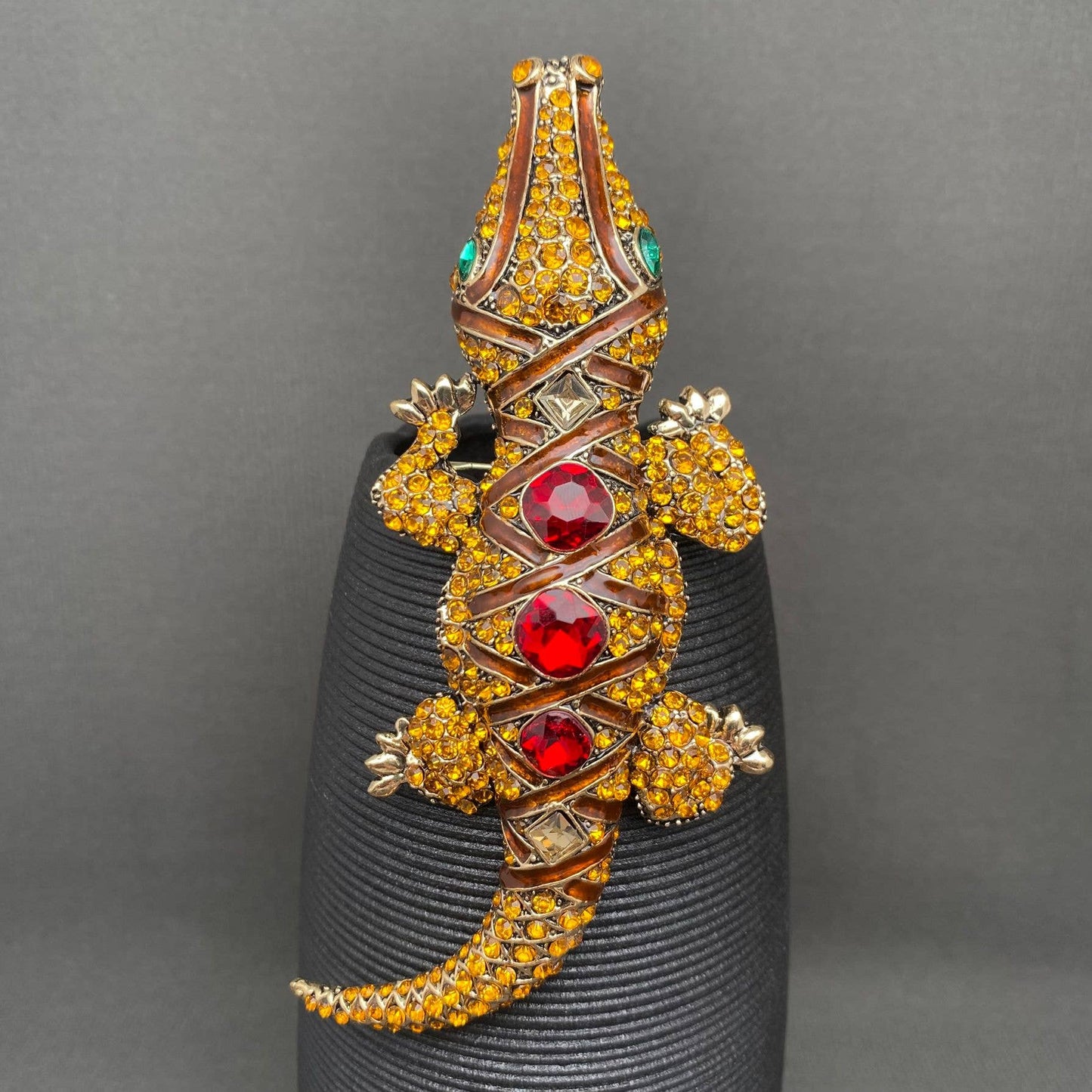 Jeweled crocodile brooch on a black stand against a gray background