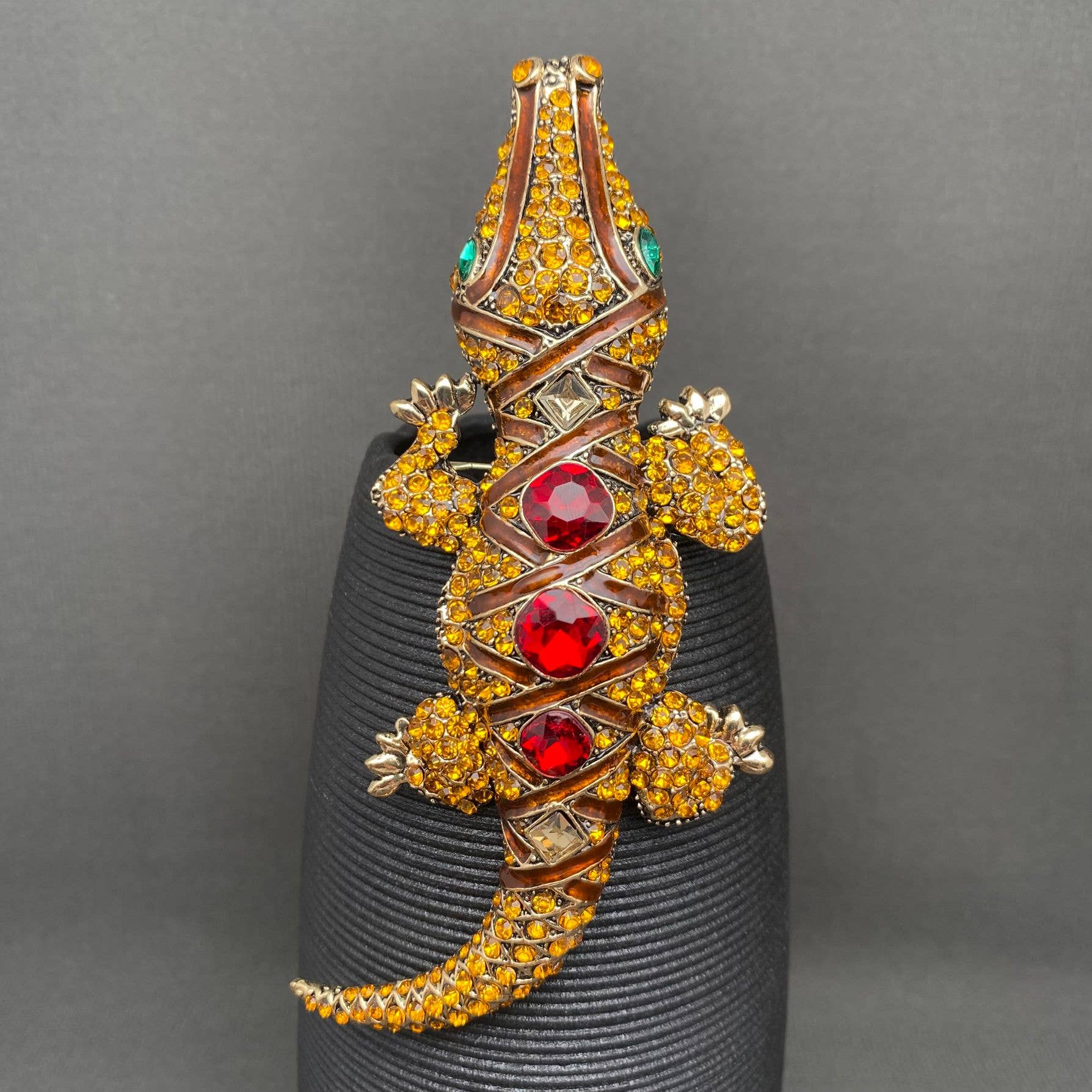 Jeweled crocodile brooch on a black stand against a gray background