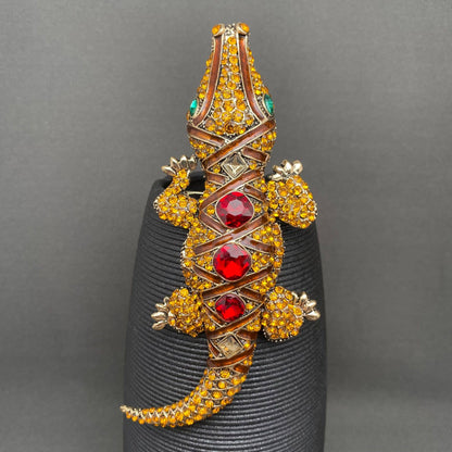 Jeweled crocodile brooch on a black stand against a gray background