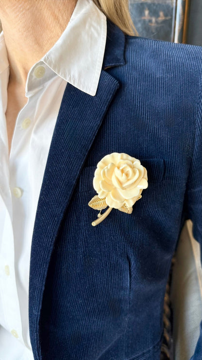 Navy blazer with an ivory and gold rose brooch worn by a person.