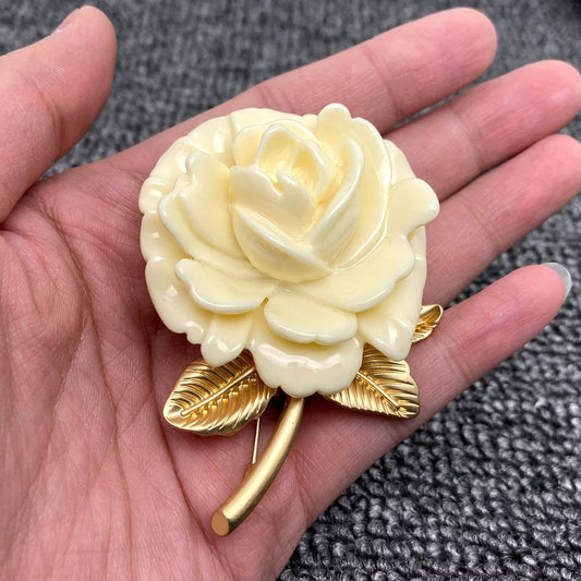 Hand holding a decorative white rose with gold leaves against a textured gray background