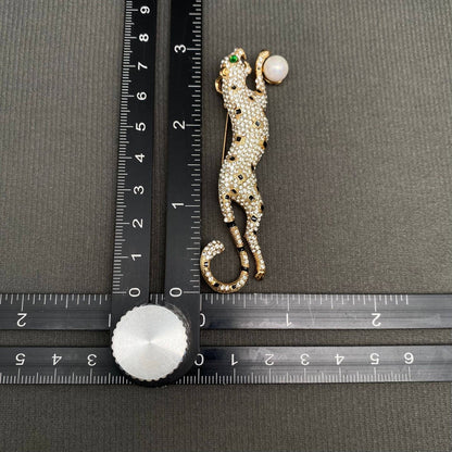 Decorative leopard brooch with gemstones next to a ruler on a gray background