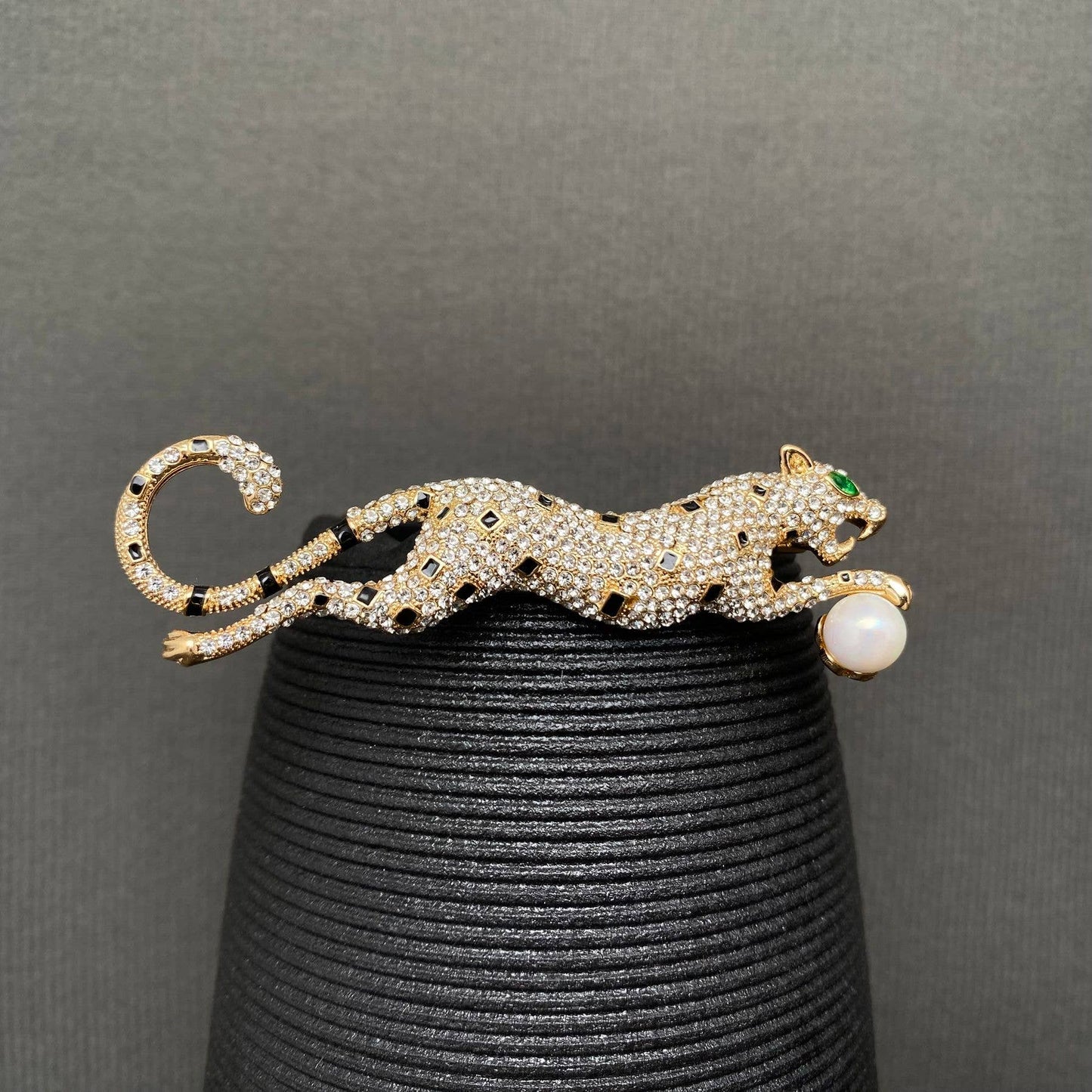Gold leopard brooch with gemstones on a black stand against a gray background