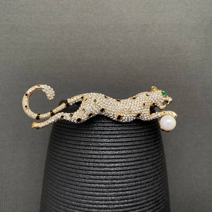 Gold leopard brooch with gemstones on a black stand against a gray background