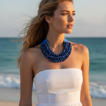 A woman wearing a blue beaded necklace and white strapless dress in an outdoor beach setting