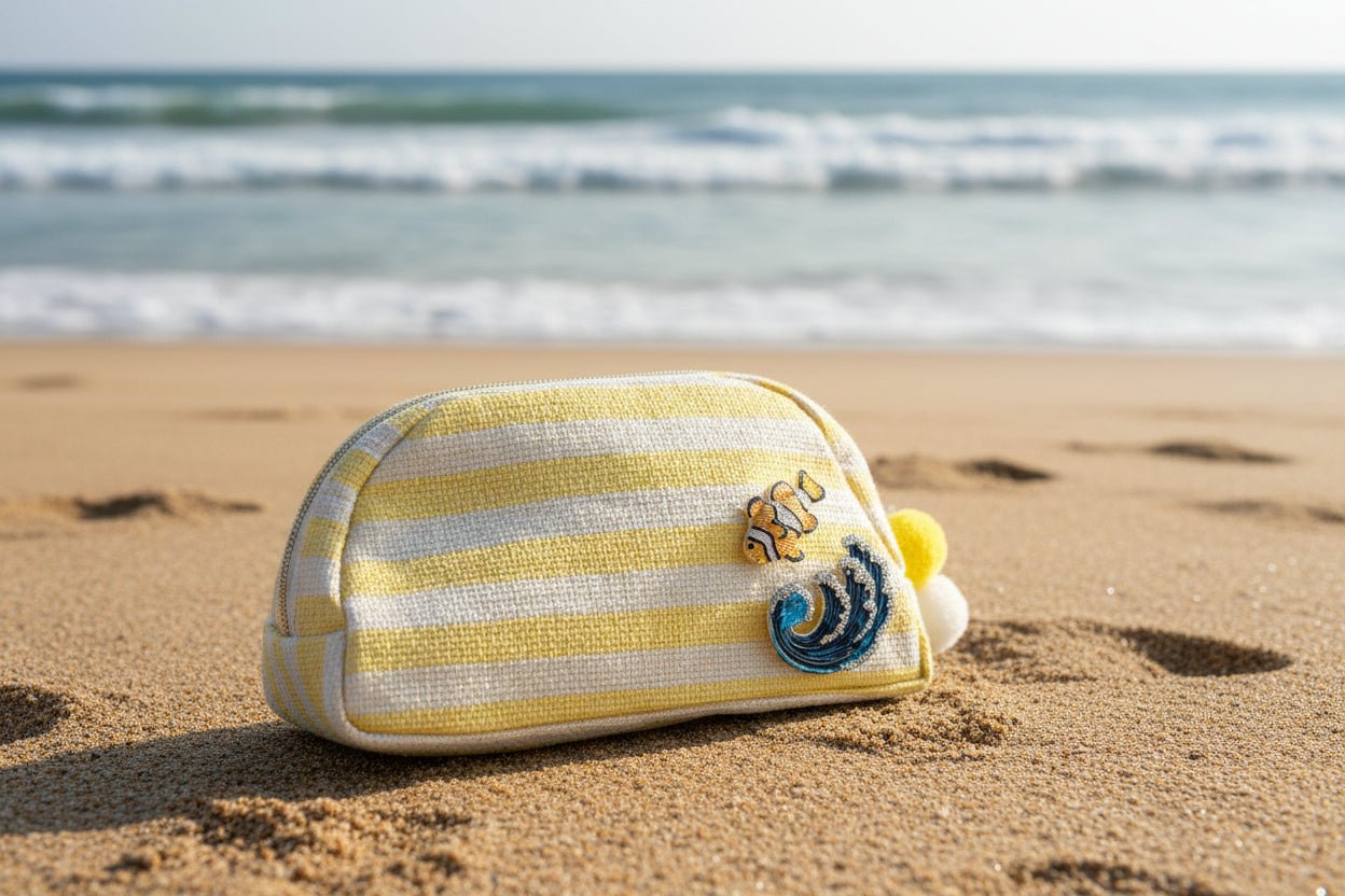 Yellow and white striped pouch with 2 ocean themed brooches on the sand at the beach.