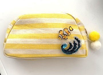 Yellow and white striped pouch with two ocean themed brooches on a white background