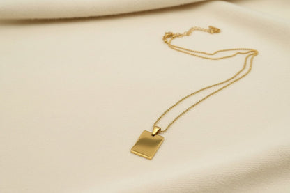 back view of a dog tag style gold necklace  with an ivory fabric background