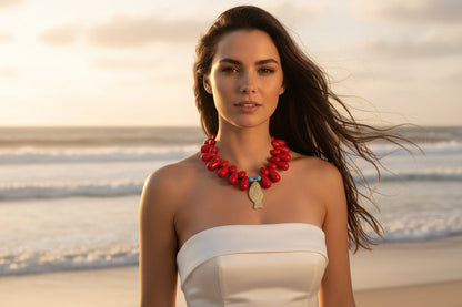 woman in a white strapless dress with a red beaded necklace and gold etched fish pendant standing on the beach