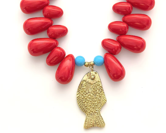 gold fish pendant necklace surrounding by two turquoise round beads and red oblong shaped beads against a white background