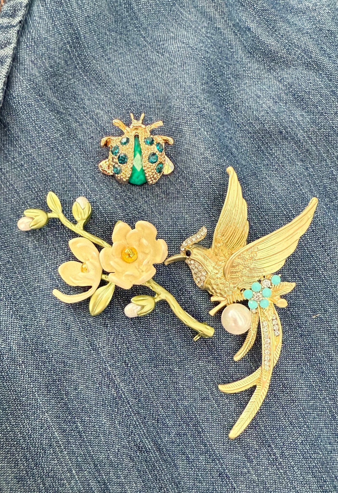 set of 3 brooches including a magnolia brand, songbird, and lady bug on a denim fabric background