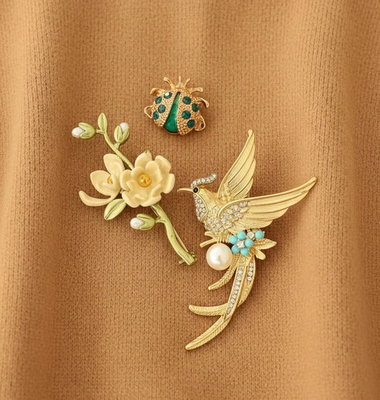 set of 3 brooches including a magnolia brand, songbird, and lady bug against a tan colored sweater material
