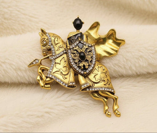 gold and black medieval knight and horse themed brooch against an ivory fabric
