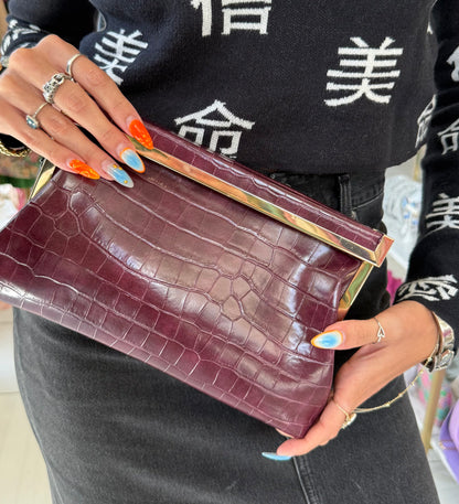 Person holding a maroon clutch with gold accents, wearing a black sweater with white characters.