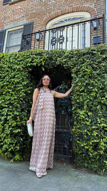 Woman in a long chevron print dress standing in front of a brick building with greenery.