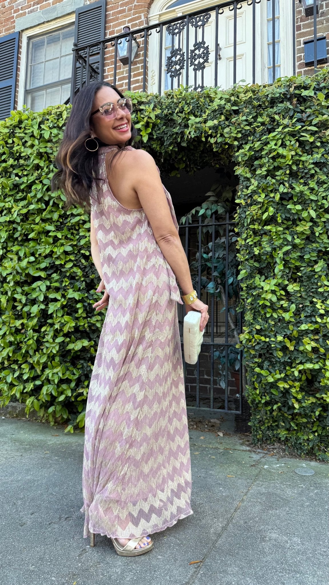 Back view of a woman in a long, chevron patterned dress standing in front of a green hedge.