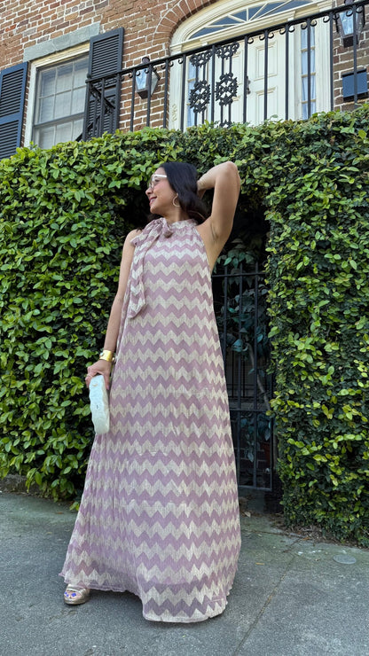 Woman in a long chevron-patterned dress standing in front of a building with greenery.