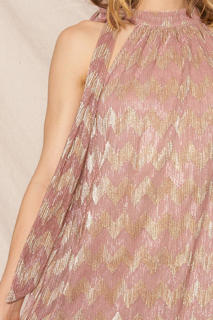 A woman wearing a metallic chevron print halter neck maxi dress with sleeveless design, standing in front of an ivory background