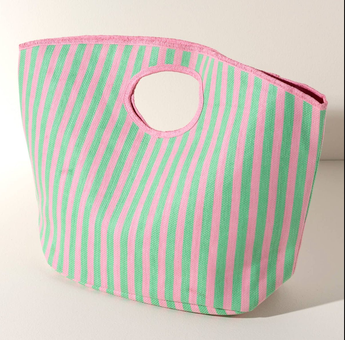 A striped tote bag with pink and green lines, featuring a flat handle against an ivory background