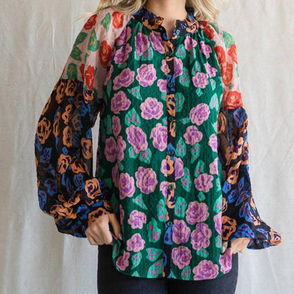 A woman wearing a colorful floral print blouse with a ruffled neckline and long balloon sleeves.