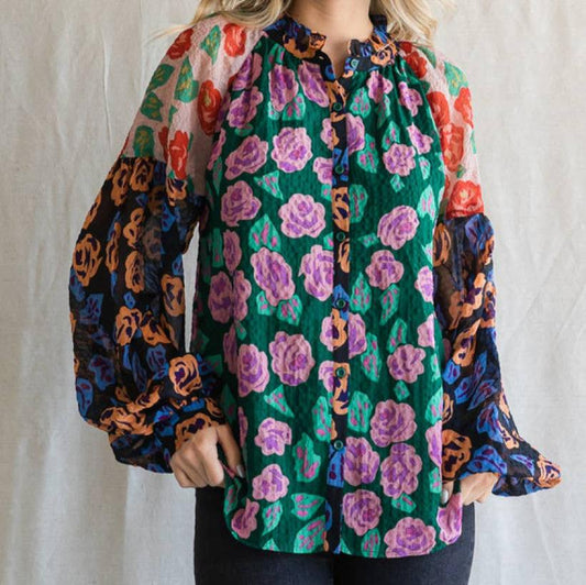 A woman wearing a colorful floral print blouse with a ruffled neckline and long balloon sleeves.