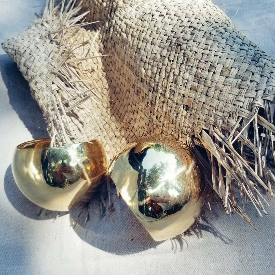 A pair of brass dome shaped cuffs sitting on tan colored raffia fabric