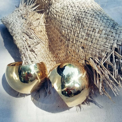 A pair of brass dome shaped cuffs sitting on tan colored raffia fabric