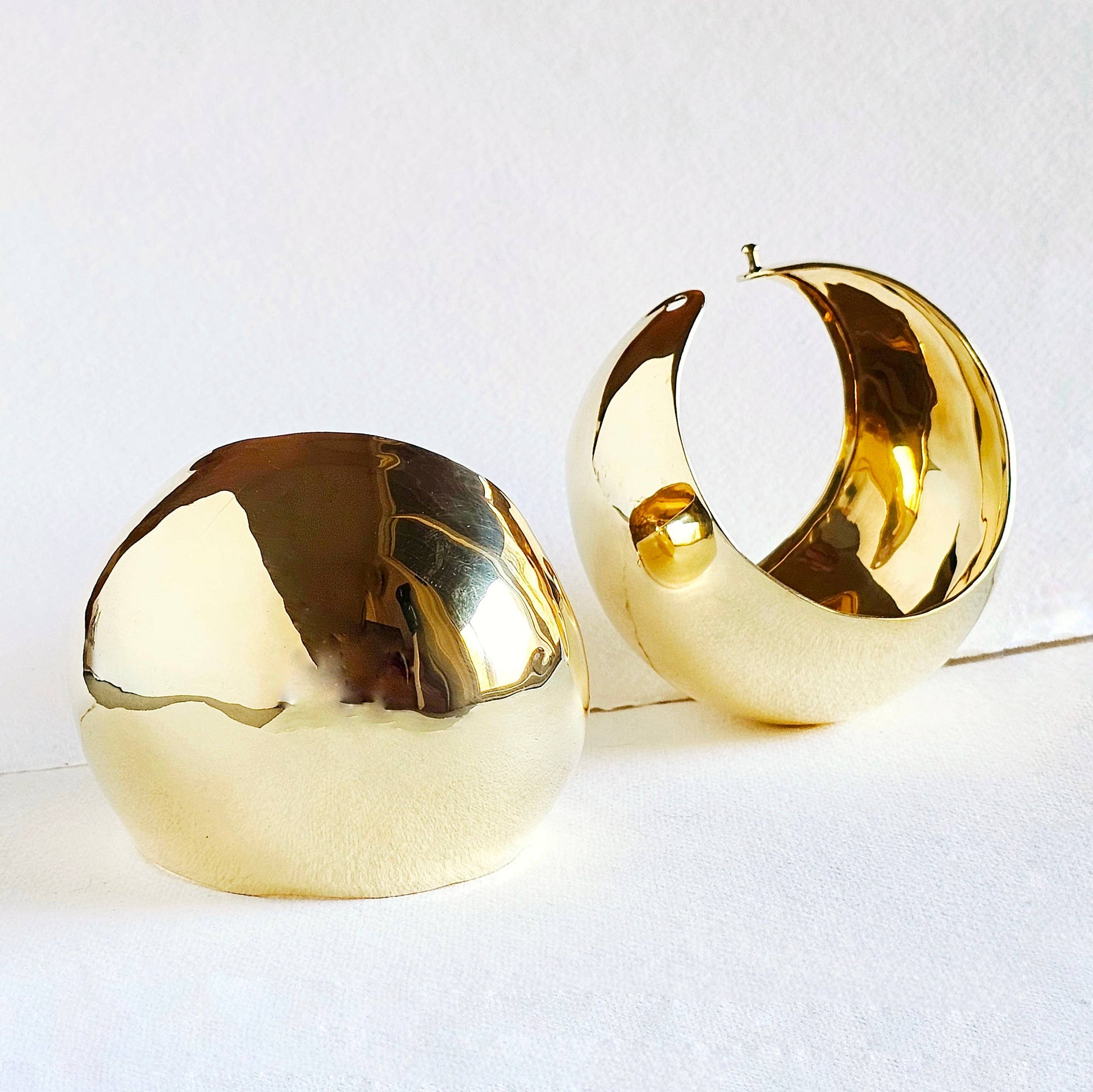 A pair of brass done shaped cuffs against a white background 
