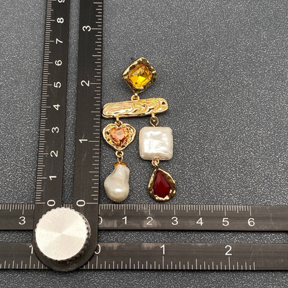 a multi stone baroque pearl earring next to a ruler for scale against a grey background