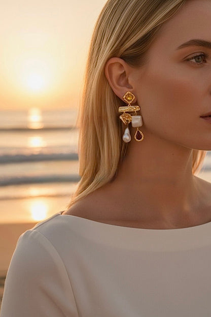 Woman wearing gold and pearl dangle earrings with a sunset over water in the background