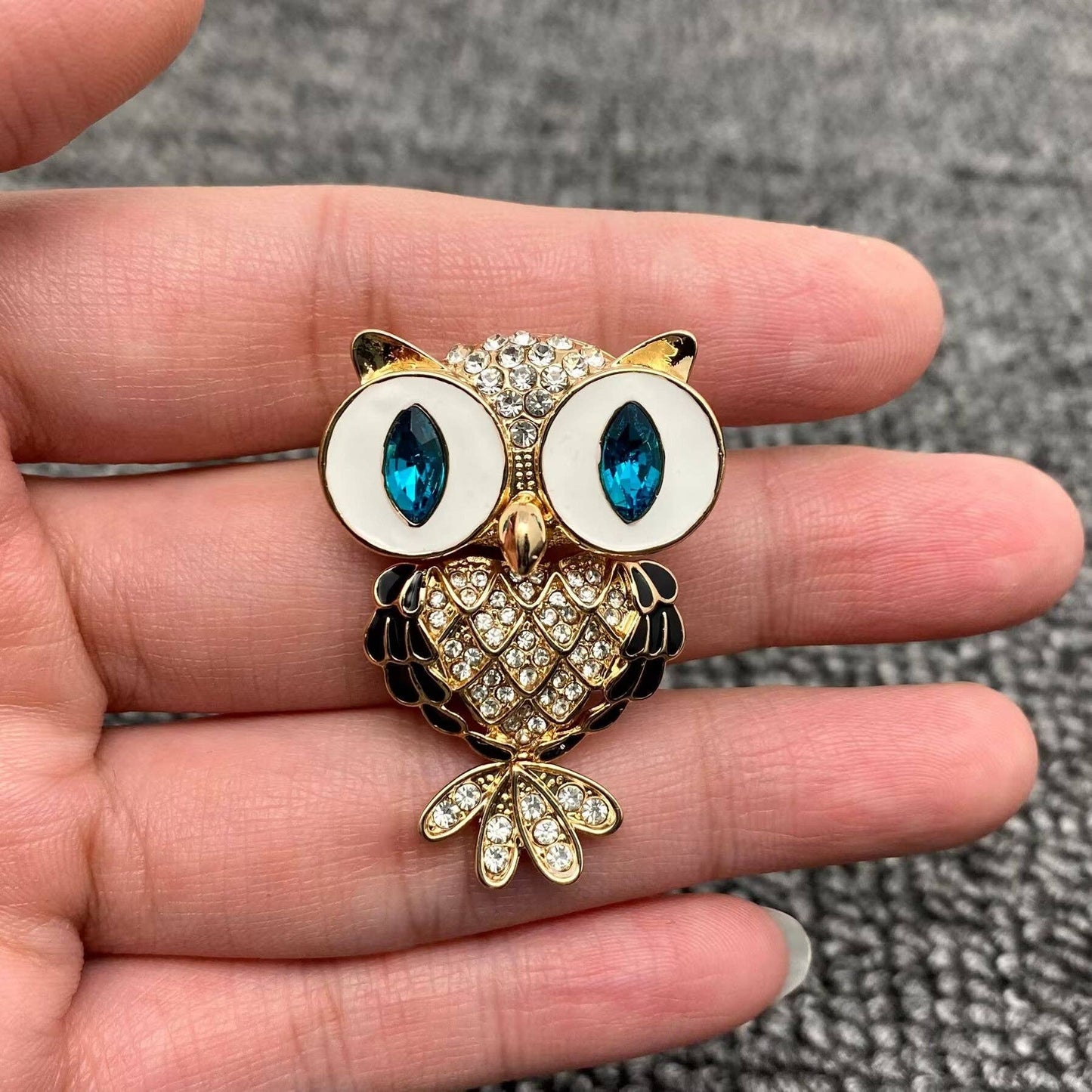 Gold owl brooch with blue gemstones held between fingers on a textured surface