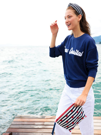 Woman holding crab and navy stripe zip pouch showing scale and embroidered crab detail — lifestyle view