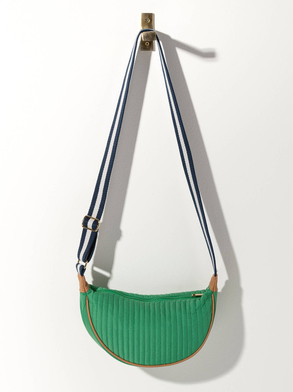 A green quilted crossbody bag with a black striped strap and a metal buckle, hanging against a white background.