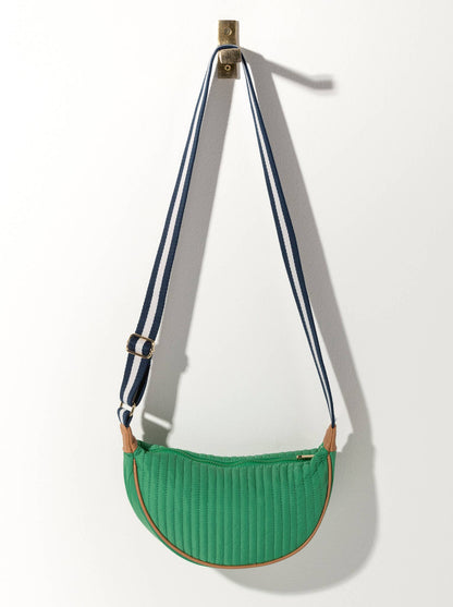 A green quilted crossbody bag with a black striped strap and a metal buckle, hanging against a white background.