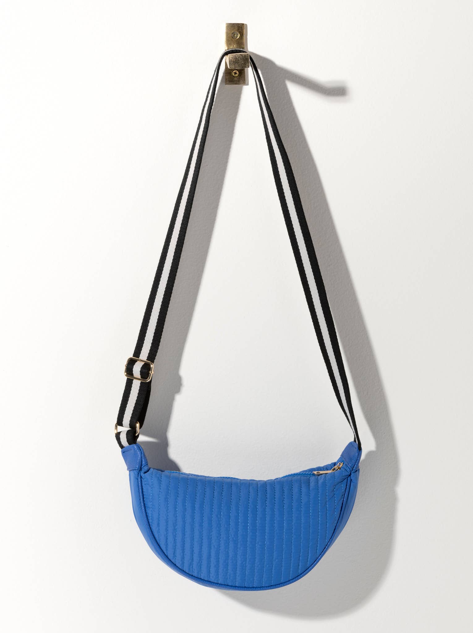 A quilted cross body bag with a striped black strap and a blue body, displayed against a white background.