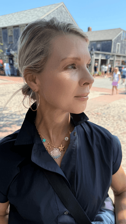 Woman wearing a dark blue shirt with a gold necklace with ocean charms, standing outdoors.