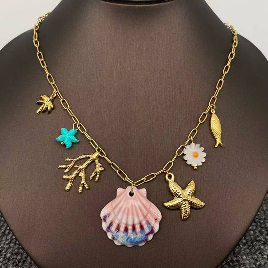 ocean themed multi charm necklace with 7 charms and central ceramic hand painted clam shell on gold chain against a black necklace stand.