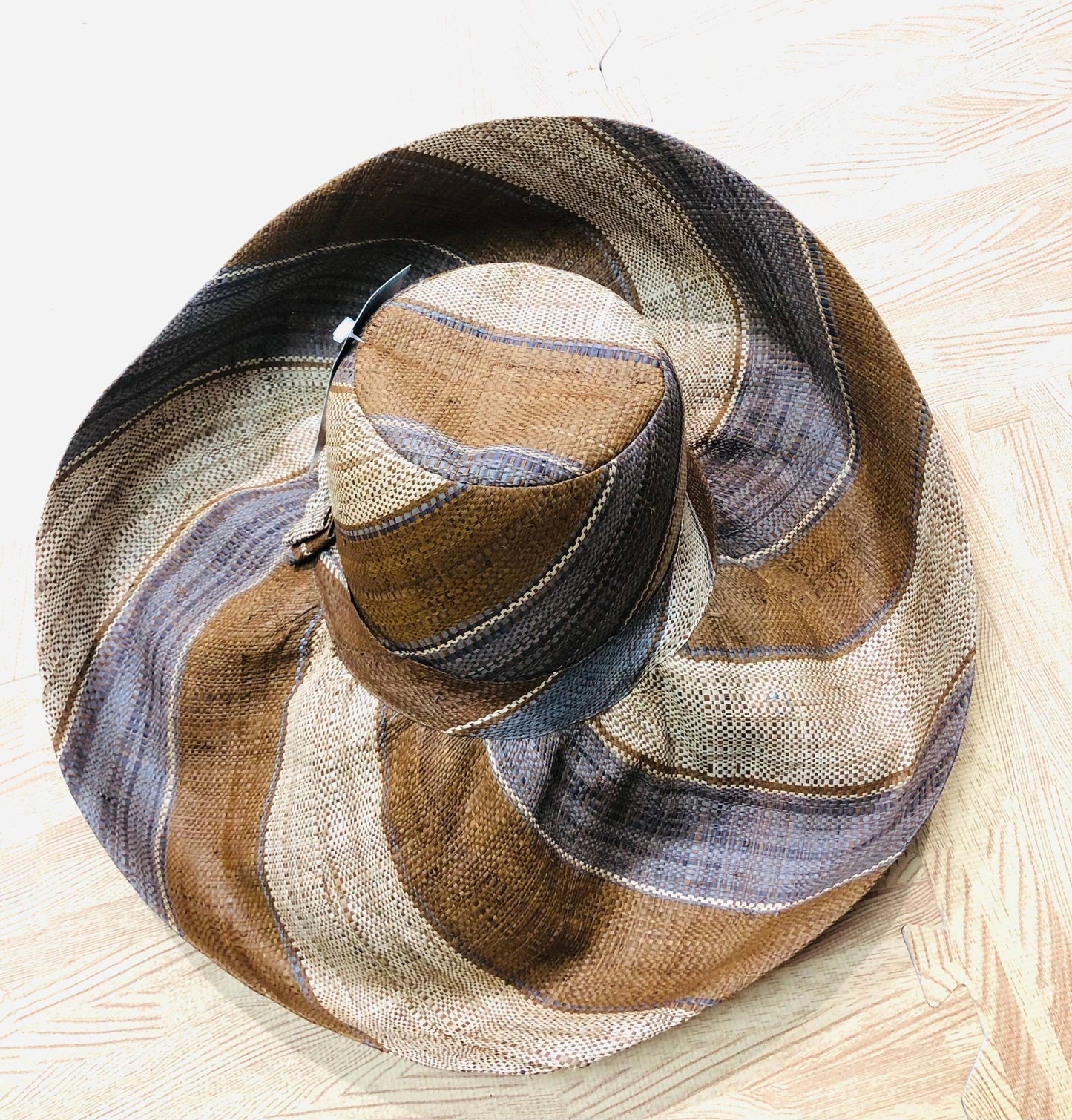 Woven hat with brown and grey striped pattern on a light wooden surface