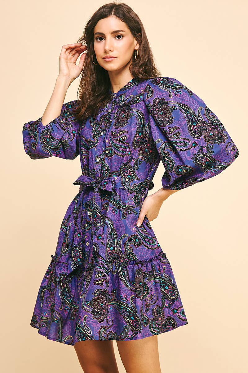 Woman wearing a purple paisley dress on a beige background