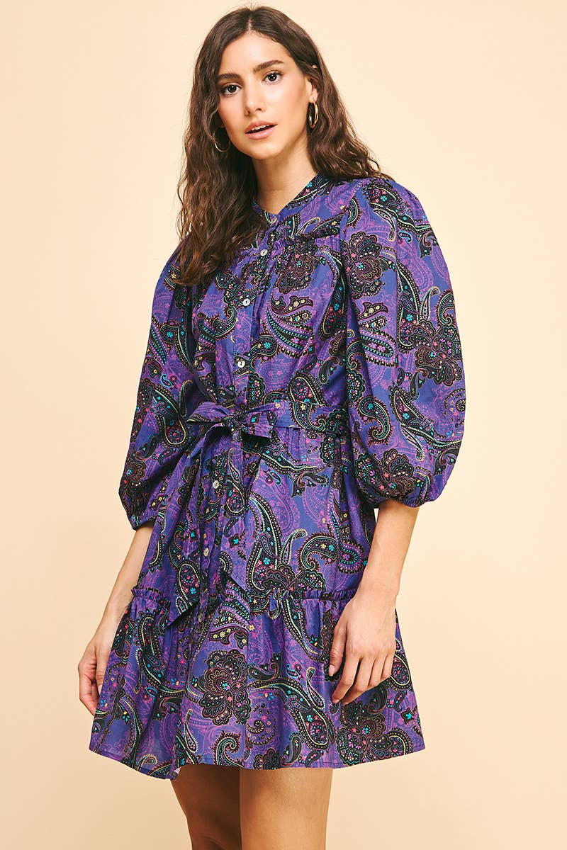 Woman wearing a purple paisley dress on a beige background