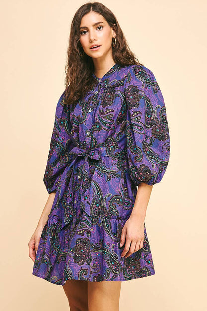 Woman wearing a purple paisley dress on a beige background