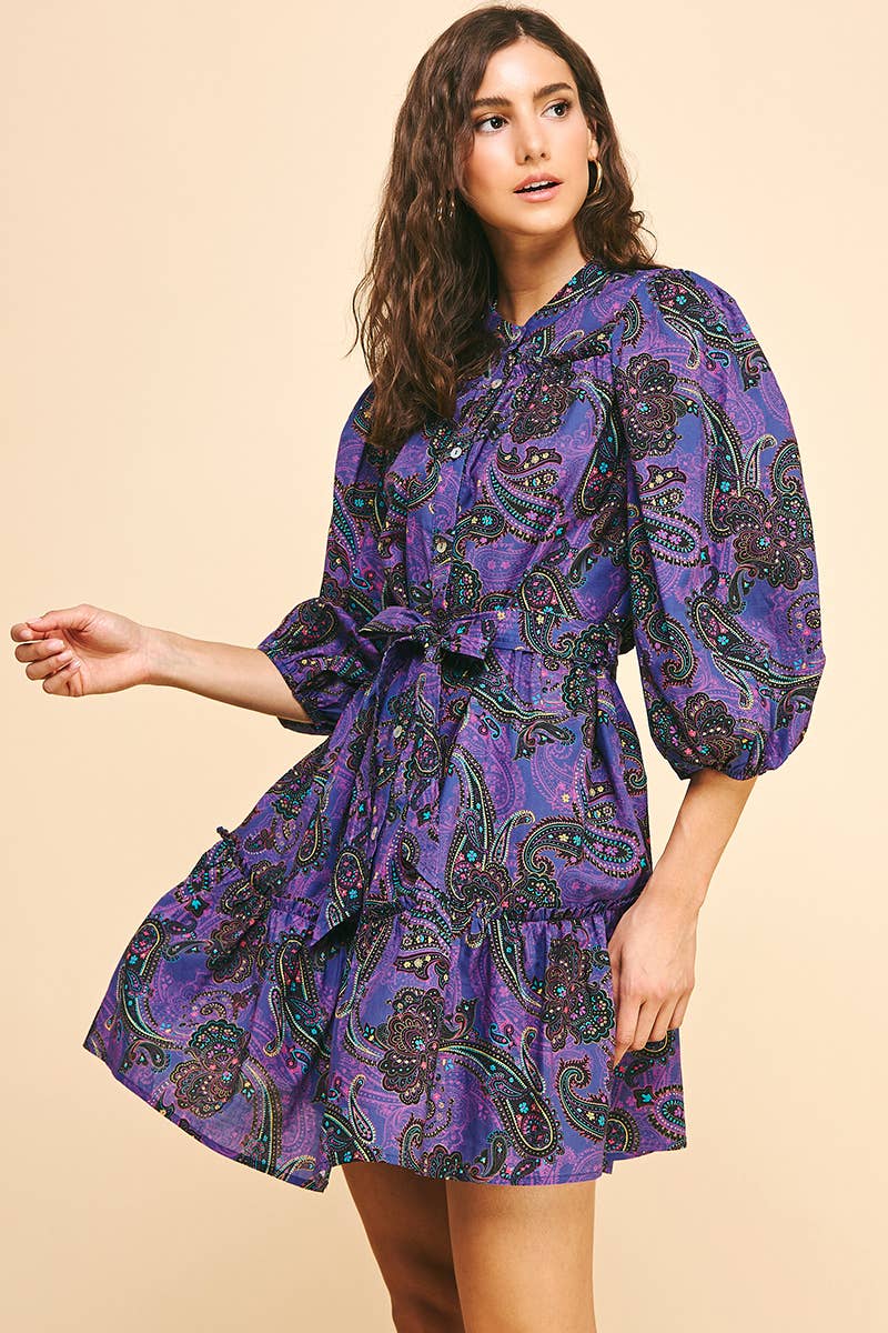Woman wearing a purple paisley dress on a beige background