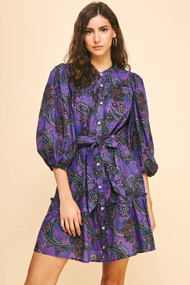 Woman wearing a purple paisley dress on a beige background