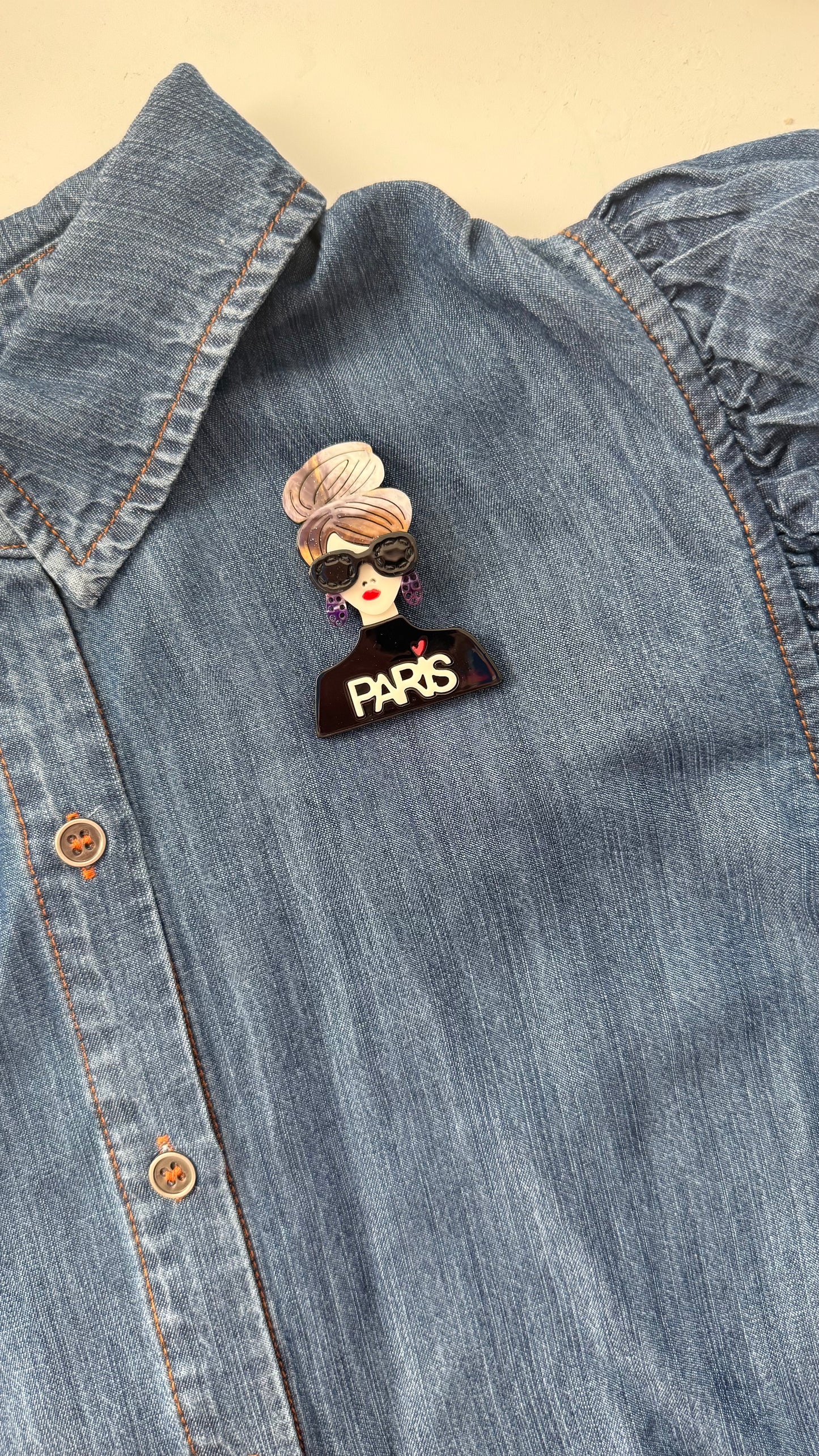 Brooch with a woman's face and 'PARIS' text on a denim shirt.