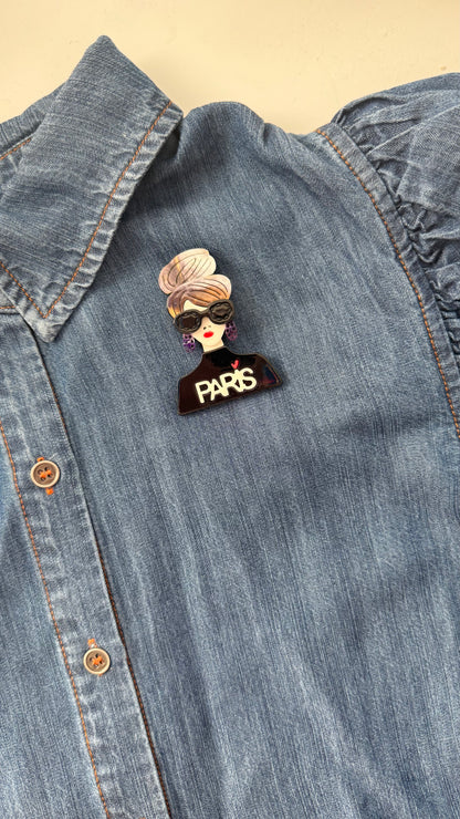 Brooch with a woman's face and 'PARIS' text on a denim shirt.